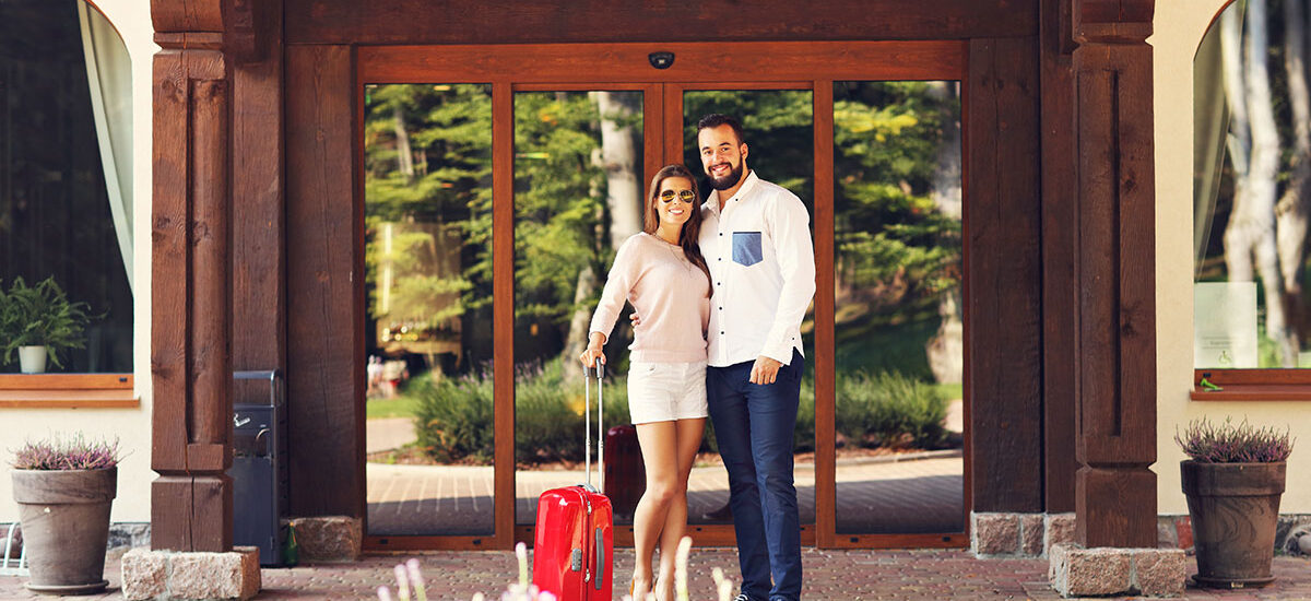 A couple with luggage at a hotel entrance.