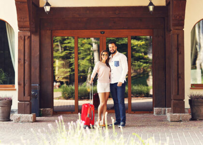 A couple with luggage at a hotel entrance.