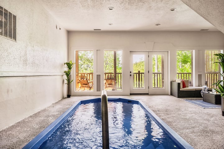 Indoor pool with balcony view and cozy living area.